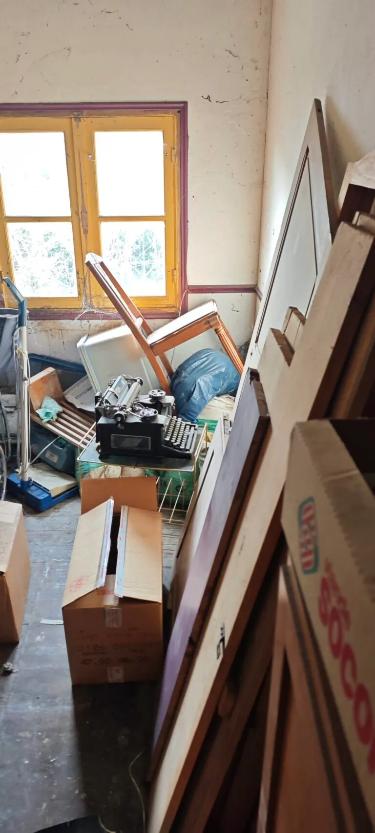 Meubles, cartons et planches accumulés près de la fenêtre avant le débarras