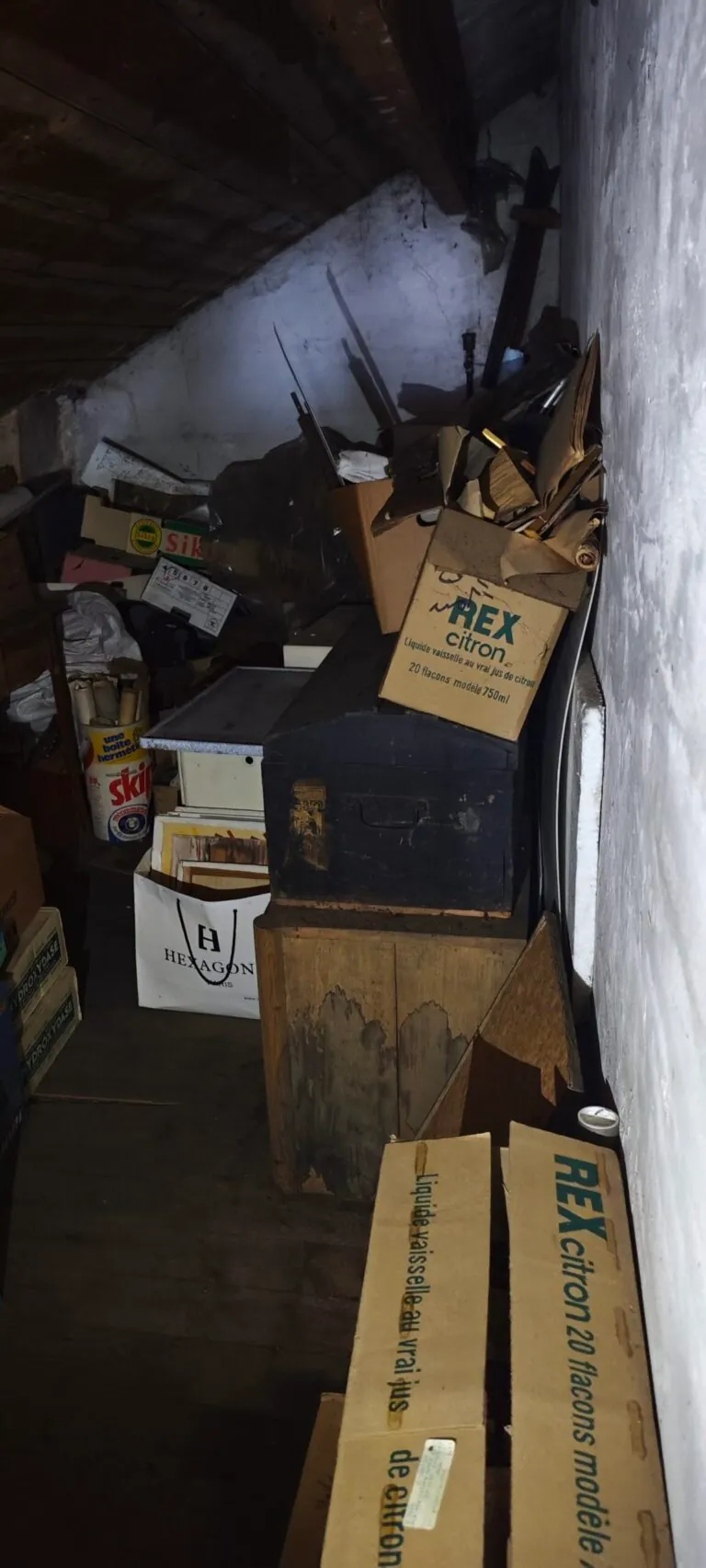 Cartons et coffres accumulés dans une pièce sous combles avant le débarras